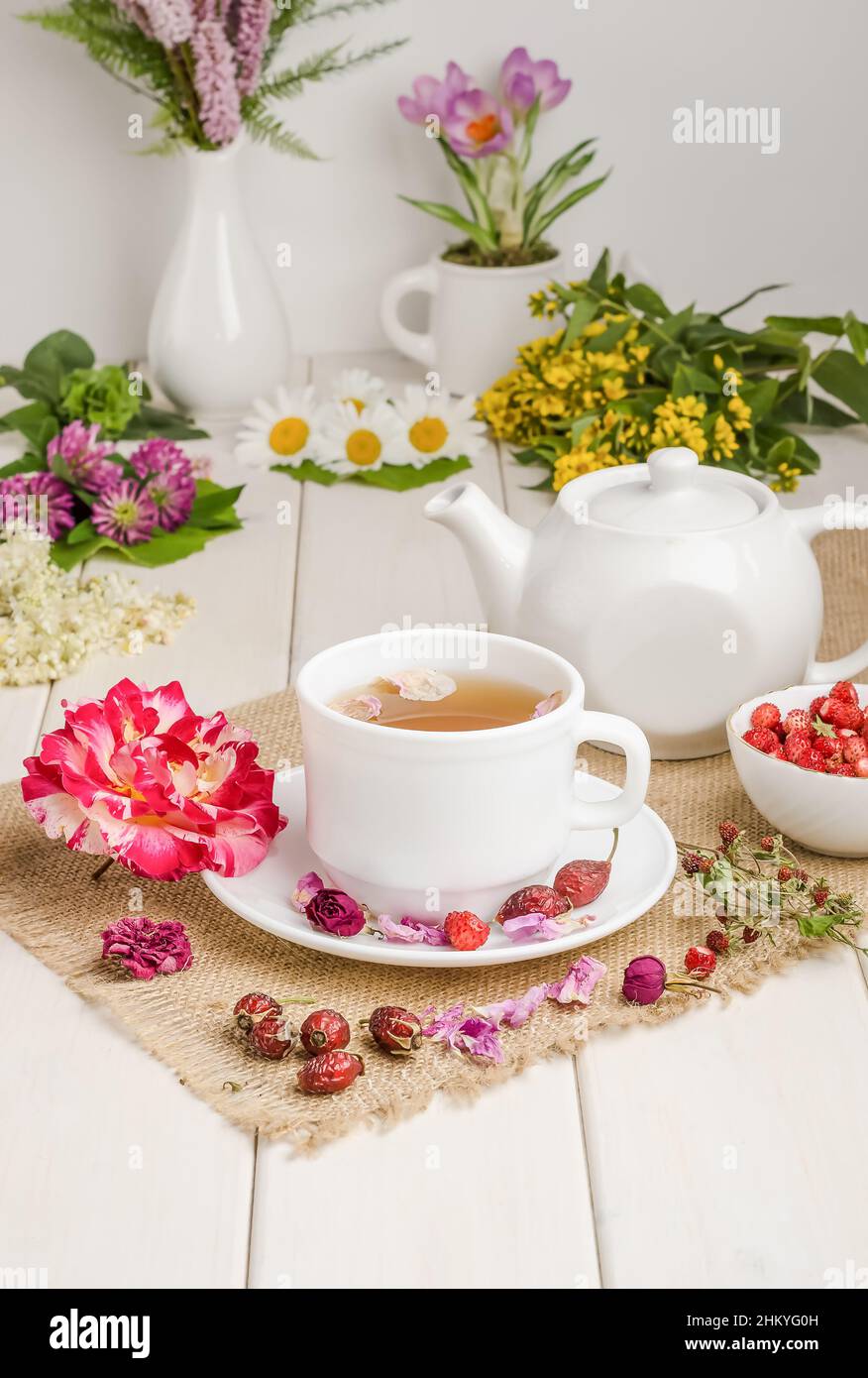 Herbal tea with rosehip, chamomile and meadowsweet in a white cup on a white wooden table with flowers. Stock Photo