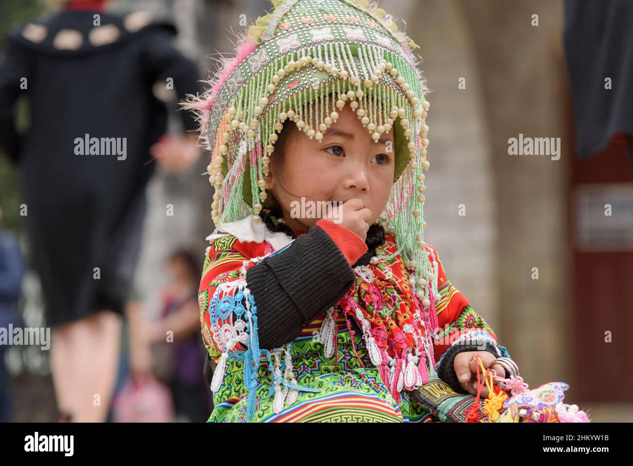 A young girl, wearing traditional Hmong tribe clothing, waits to pose for photographs by tourists in the town square, Sapa (Sa Pa), Lao Cai, Vietnam Stock Photo
