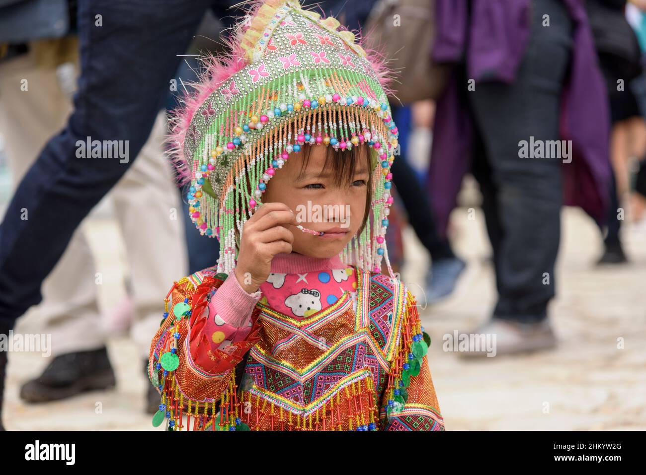 A young girl, wearing traditional Hmong tribe clothing, waits to pose for photographs by tourists in the town square, Sapa (Sa Pa), Lao Cai, Vietnam Stock Photo