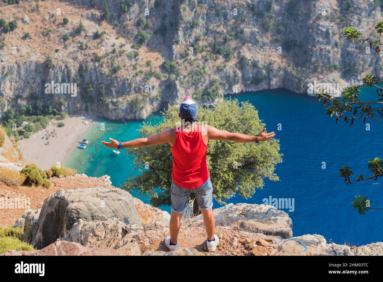 Young man standing at the edge of a cliff with open arms and enjoying the beautiful sea scenery. Stock Photo