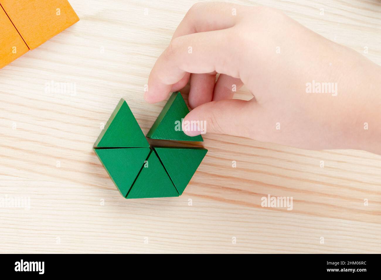 A child plays with colored blocks constructs a model on a light wooden background Stock Photo