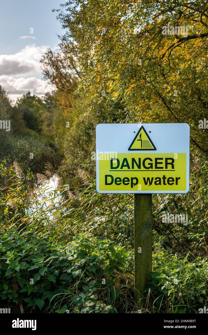 A yellow Danger Deep Water sign near an overgrown pond.  Trumpington, Cambridge, UK Stock Photo