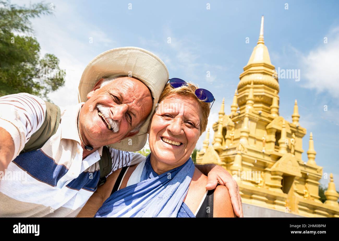 Senior couple taking selfie at golden temple in Ko Samui - Happy retired people traveling to Thailand wonders - Active elderly concept and fun around Stock Photo