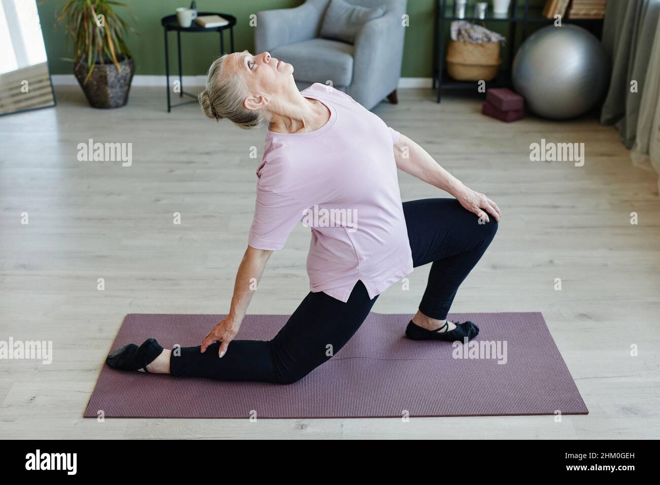 Elderly grey-haired woman looking upwards during yoga exercise while standing on mat and bending backwards Stock Photo