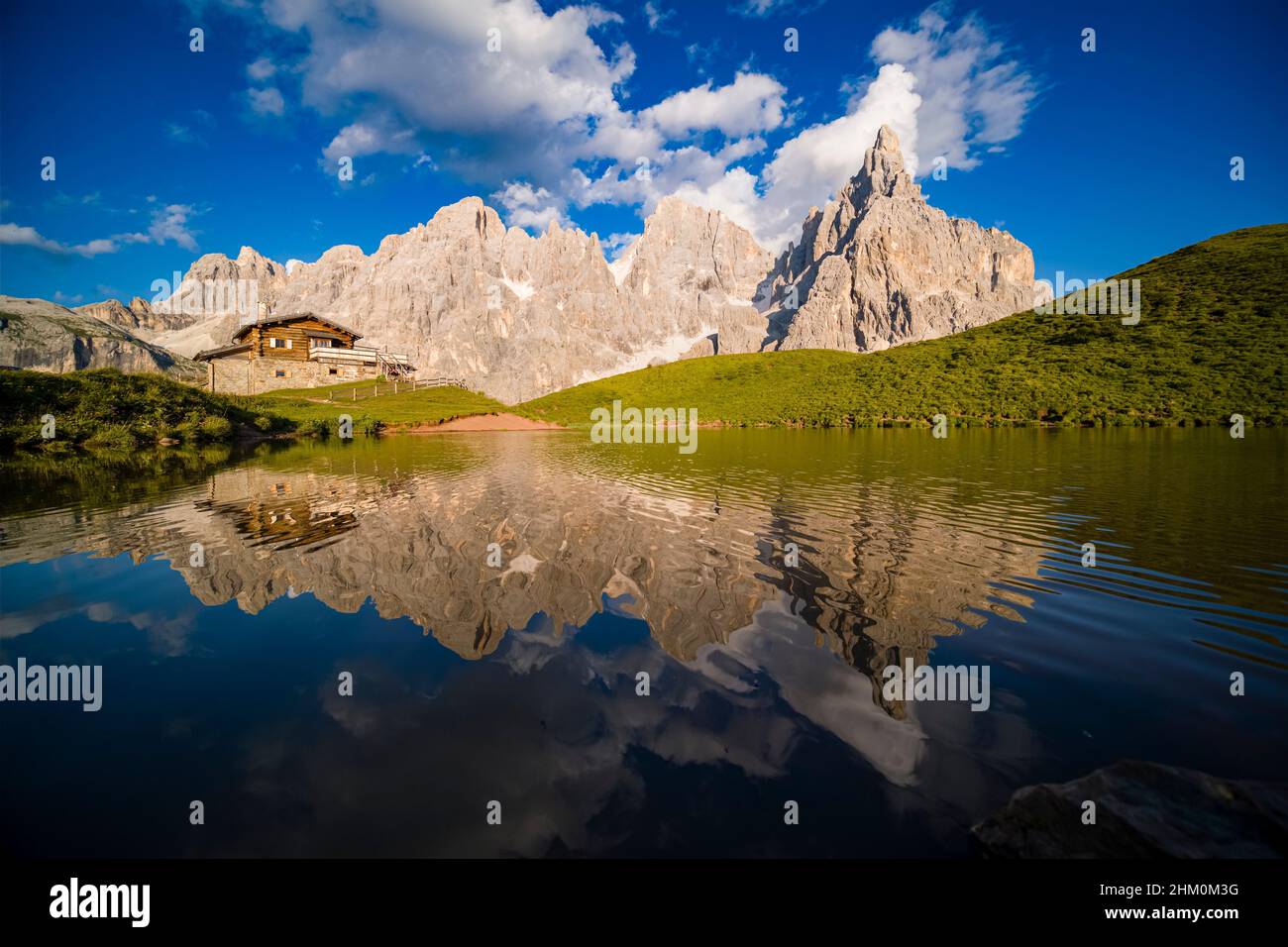 Baita Segantini, an alpine hut and summits and rock faces of the Pala group, Cimon della Pala, one of the main summits, standing out, reflecting in a Stock Photo