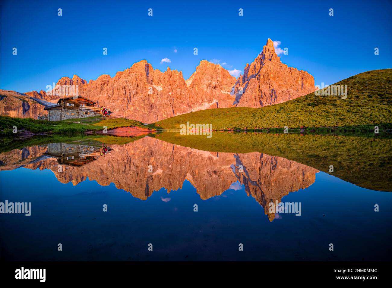 Baita Segantini, an alpine hut and summits and rock faces of the Pala group, reflecting in a lake at sunset. Stock Photo
