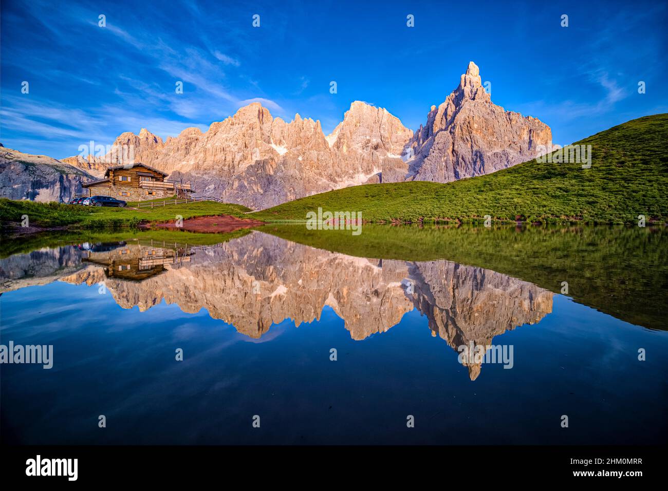 Baita Segantini, an alpine hut and summits and rock faces of the Pala group, reflecting in a lake before sunset. Stock Photo