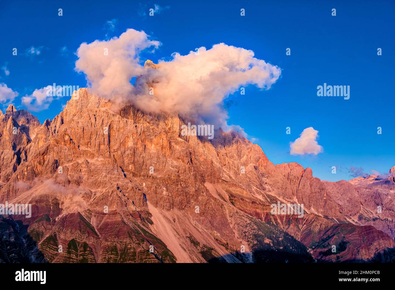 Summit and west face of Cimon della Pala, one of the main summits of the Pala group, covered in clouds, seen from above Rolle Pass at sunset. Stock Photo