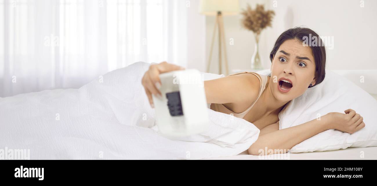 Woman looks at alarm clock and starts panicking when she realises she's overslept Stock Photo