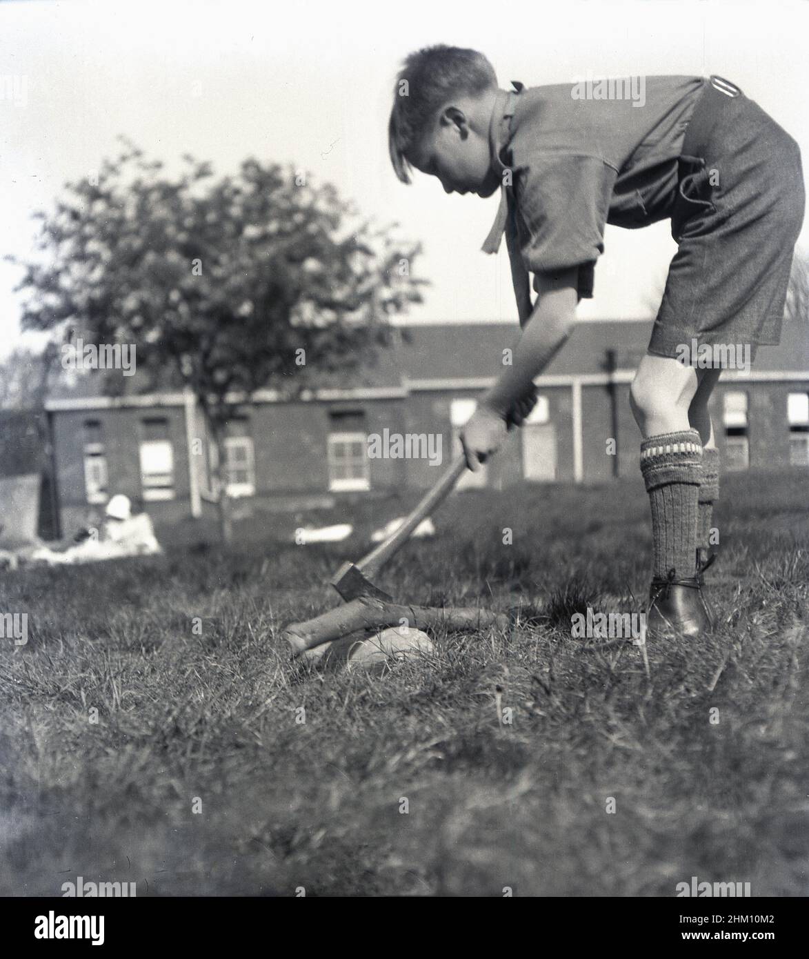 1942, historical, a cub scout in his uniform using an axe, to chop a tree branch in the grounds of Queen Mary's Hospital in Carshalton, Surrey, England, UK. Opened in 1908 as the Southern Hospital, in 1909 it became a place for the poor and sick children of London, many who had TB and was renamed the Children's Infirmary. The young patients were housed in single storey ward blocks. In 1915 it was renamed the Queen Mary's Hospital for Children when Her Majesty became its patron. During WW2, scouts who has been injured during the Blitz or were sick were sent there for treatment and to recover. Stock Photo