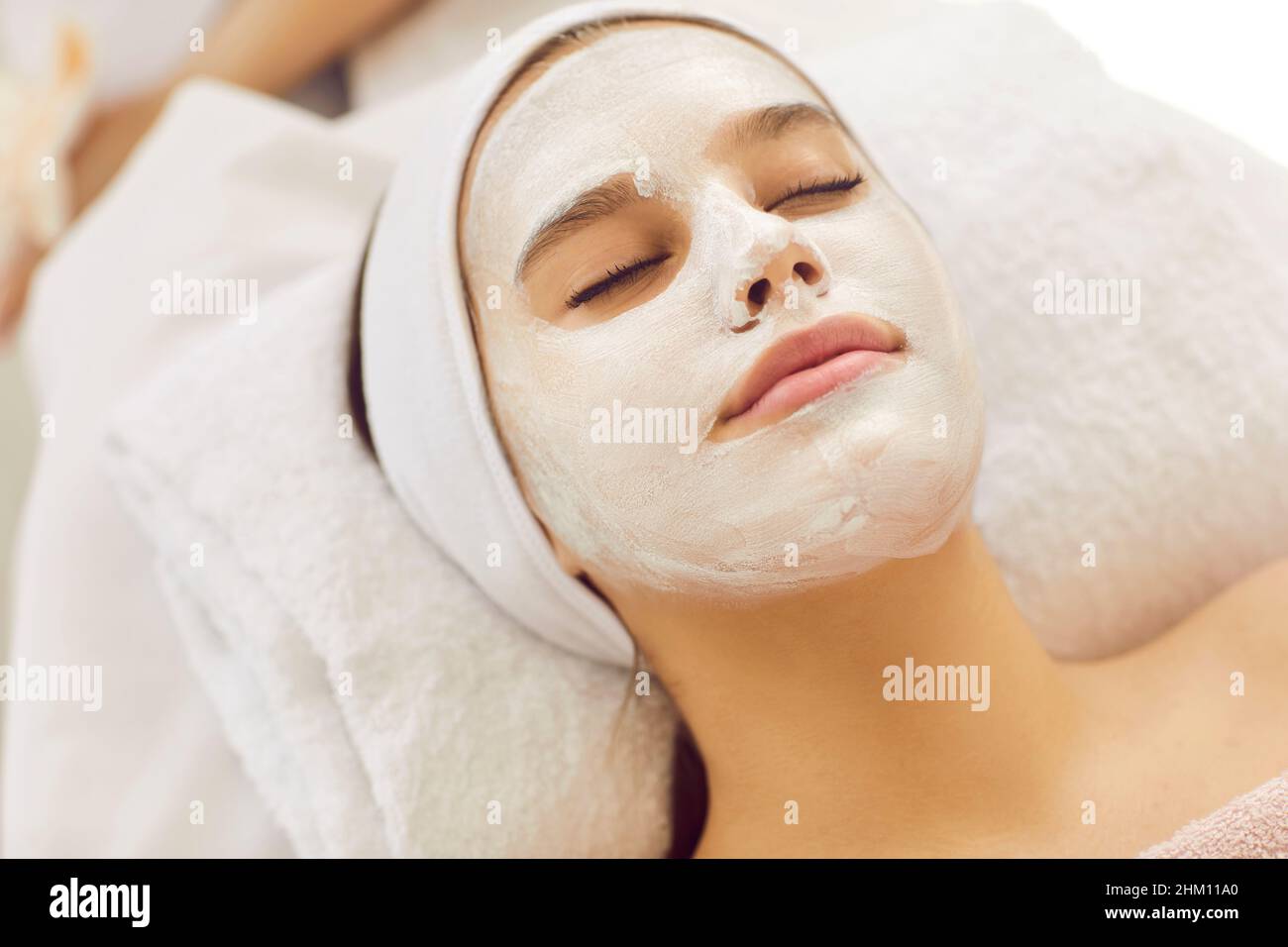 Beautiful woman in beauty salon does skin care treatments and enjoys moisturizing face mask. Stock Photo