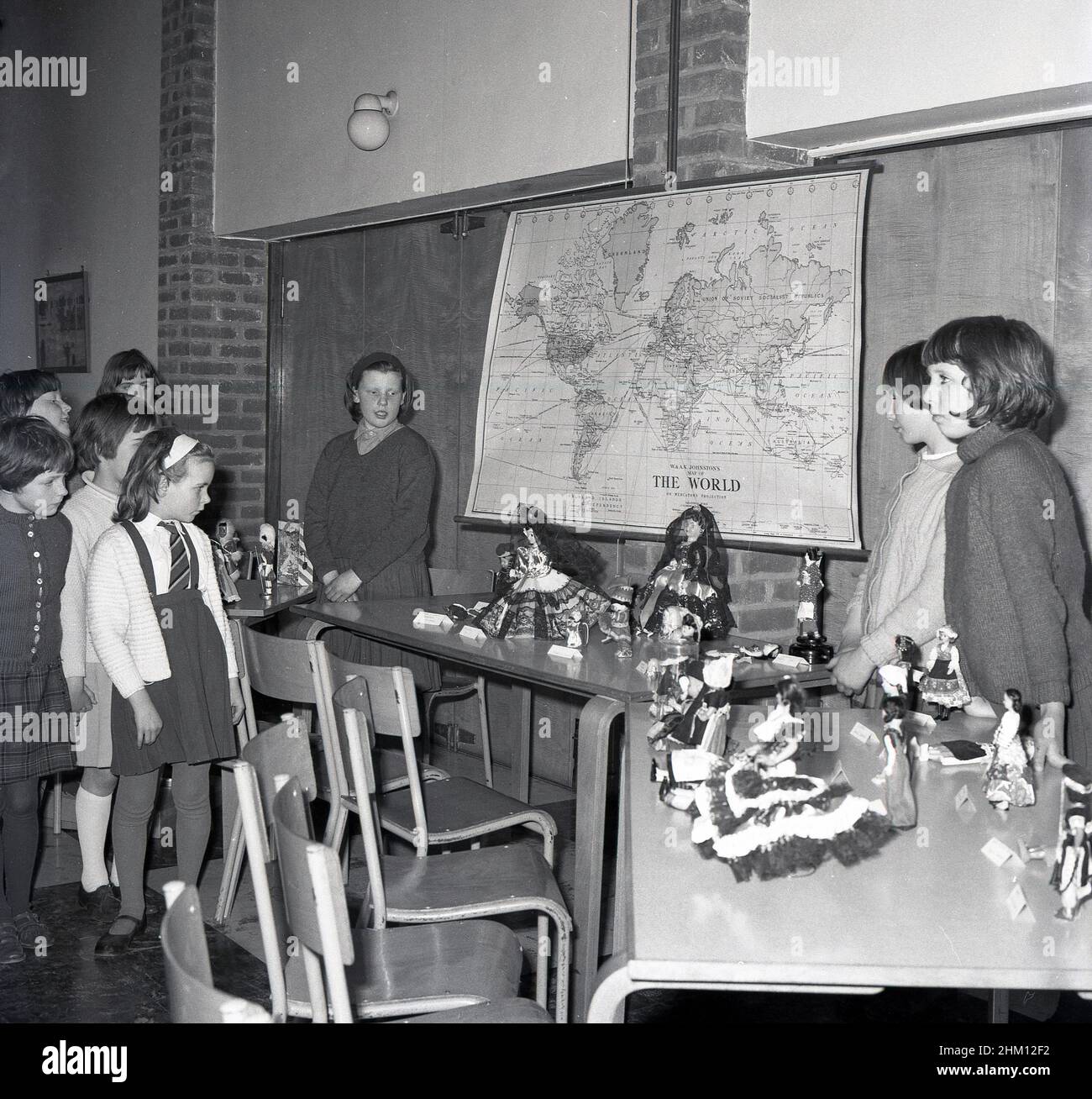 1960s, historical, primary school, dolls from different countries displayed  on tables, with world map on wall, Scotland, UK. Typically a dressed model of a human character, dolls were often used as a plaything or toy, particularly for girls, and have a history dating back to the ancient civilisations. The modern type of manufactured doll dates back to 15th century Germany. Stock Photo