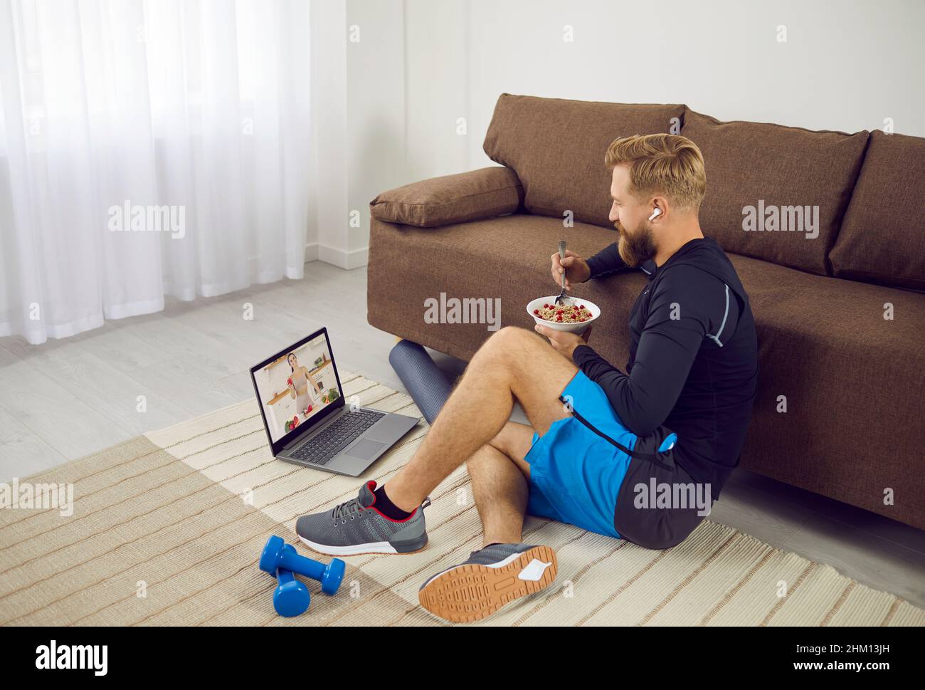 Man rests after active sports training, eats oatmeal and watches videos about proper nutrition. Stock Photo