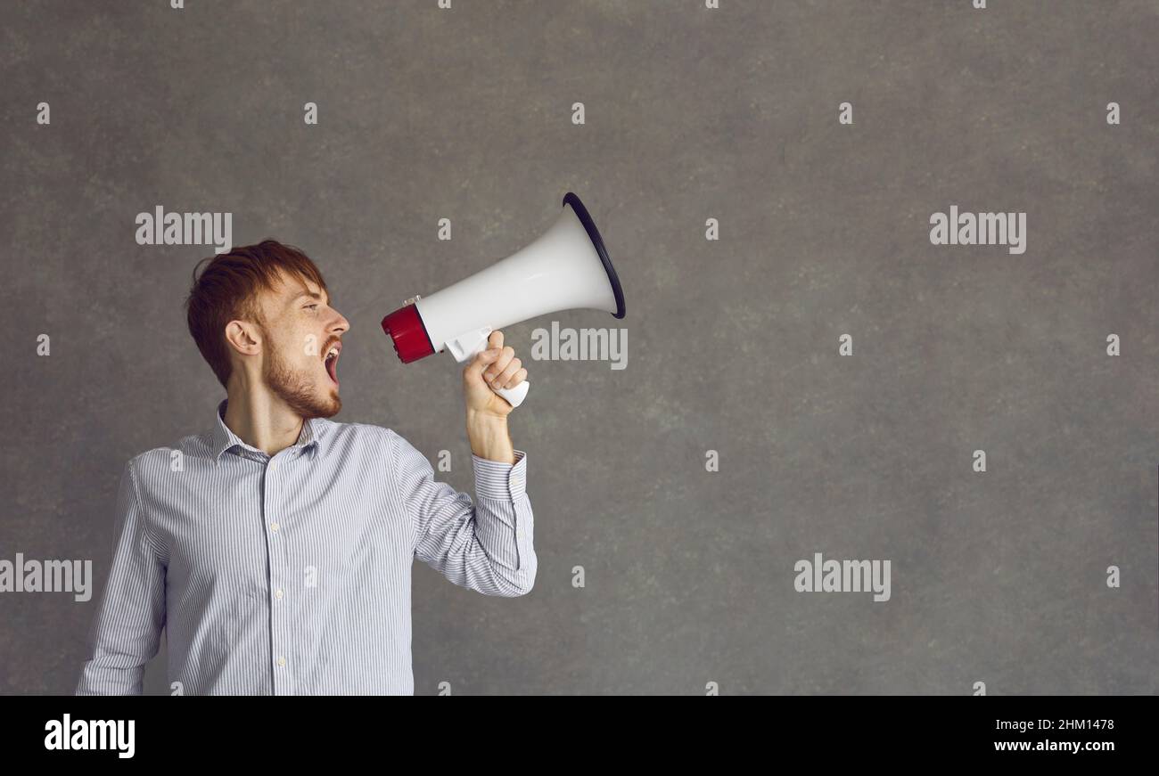 Young determined man makes a loud announcement while speaking into a loudspeaker. Stock Photo