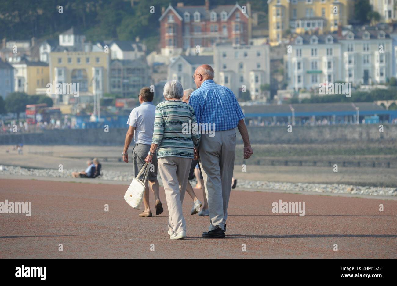 ELDERLY COUPLE WALKING ON THE SEAFRONT AT LLANDUDNO NORTH WEST WALES RE EXERCISE FITNESS HEALTH HEALTHY LIFESTYLE PENSIONERS PENSIONS ETC UK Stock Photo