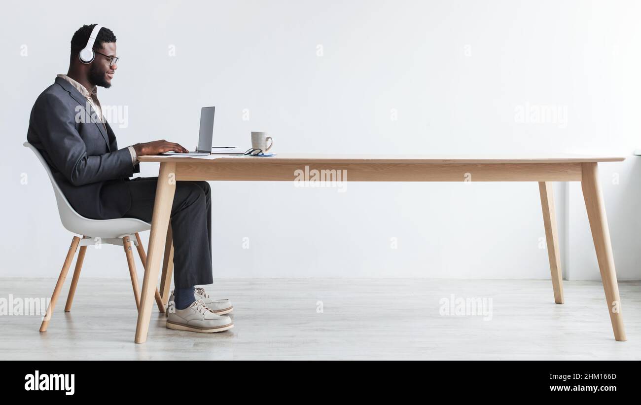 Black businessman in headphones making video call, sitting at desk, having web conference with customer at office Stock Photo