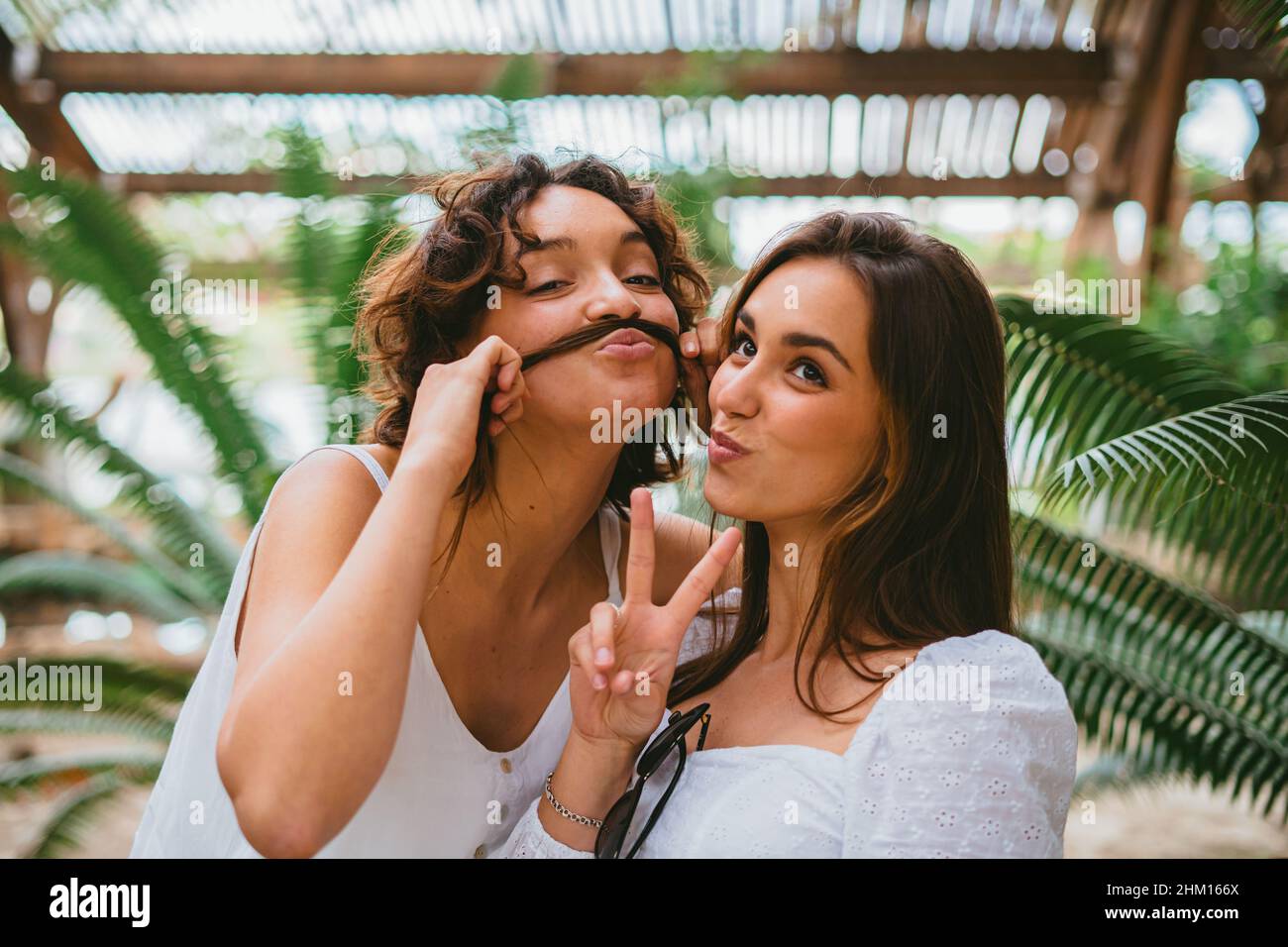 Two funny teenager girls looking at camera and smiling. One of them is playing and making