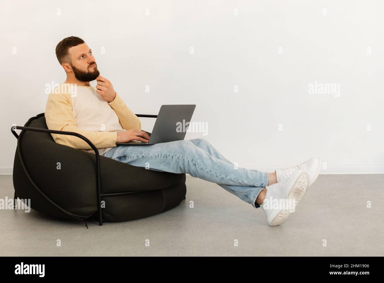 Thoughtful Man Using Laptop Thinking Sitting In Chair At Home Stock Photo