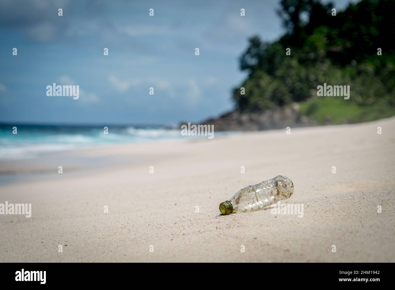 plastic rubbish washed up from ocean on sandy white beach gentle waves in paradise mountain background pollution Stock Photo
