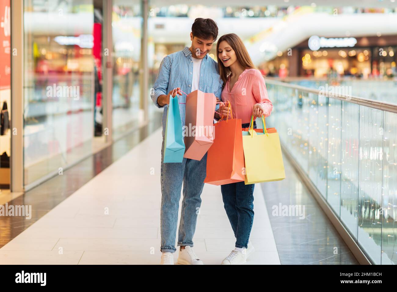 Young Spouses Shopping Holding Paper Shopper Bags Standing In Hypermarket Stock Photo