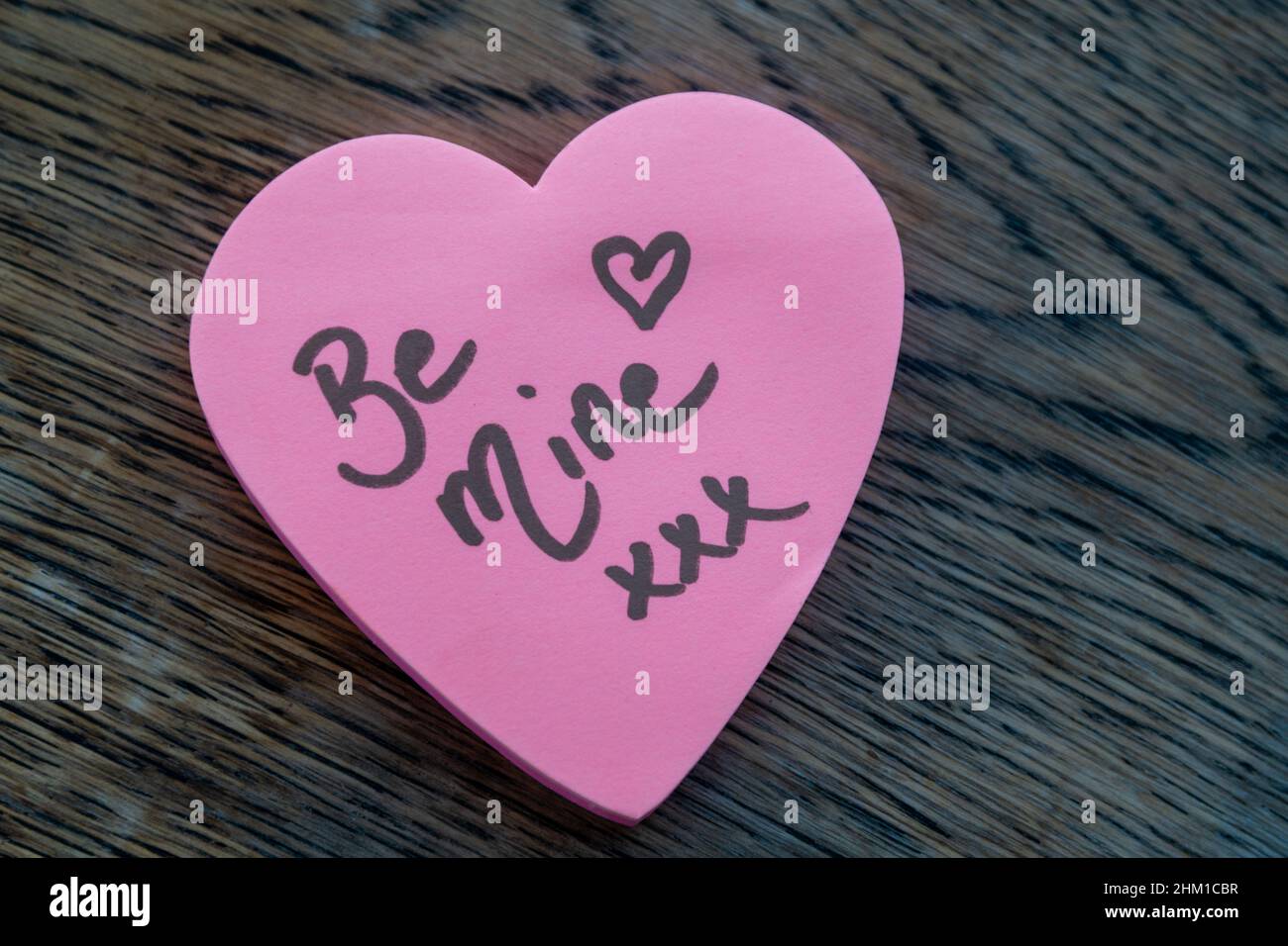Be Mine hand wrote text on pink love heart with drawn hearts. On rustic wooden background. Love Valentines concept. Stock Photo