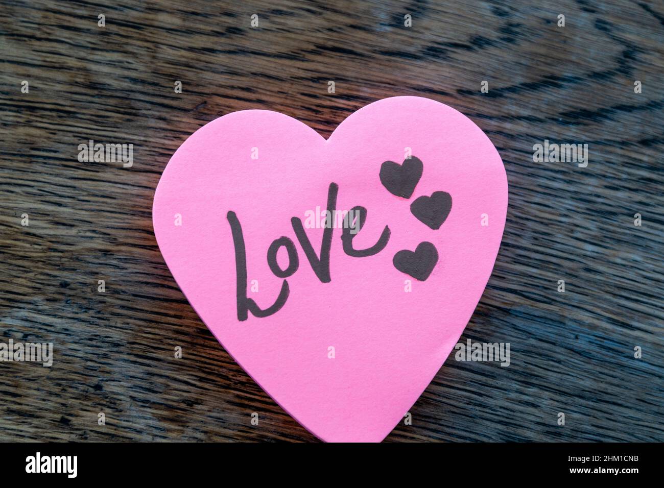 Love hand wrote text on pink love heart with drawn hearts. On rustic wooden background. Love Valentines concept. Stock Photo