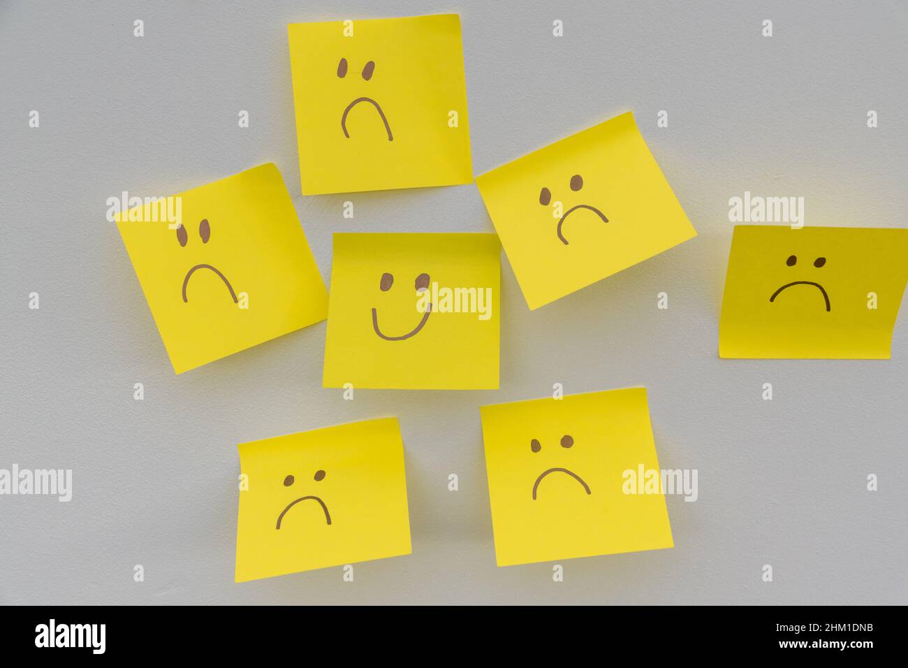 Happy smiling face amongst lots of sad faces. Hiding depression, mental health issues or anxiety concept. Two faces concepts background. Pretending fa Stock Photo