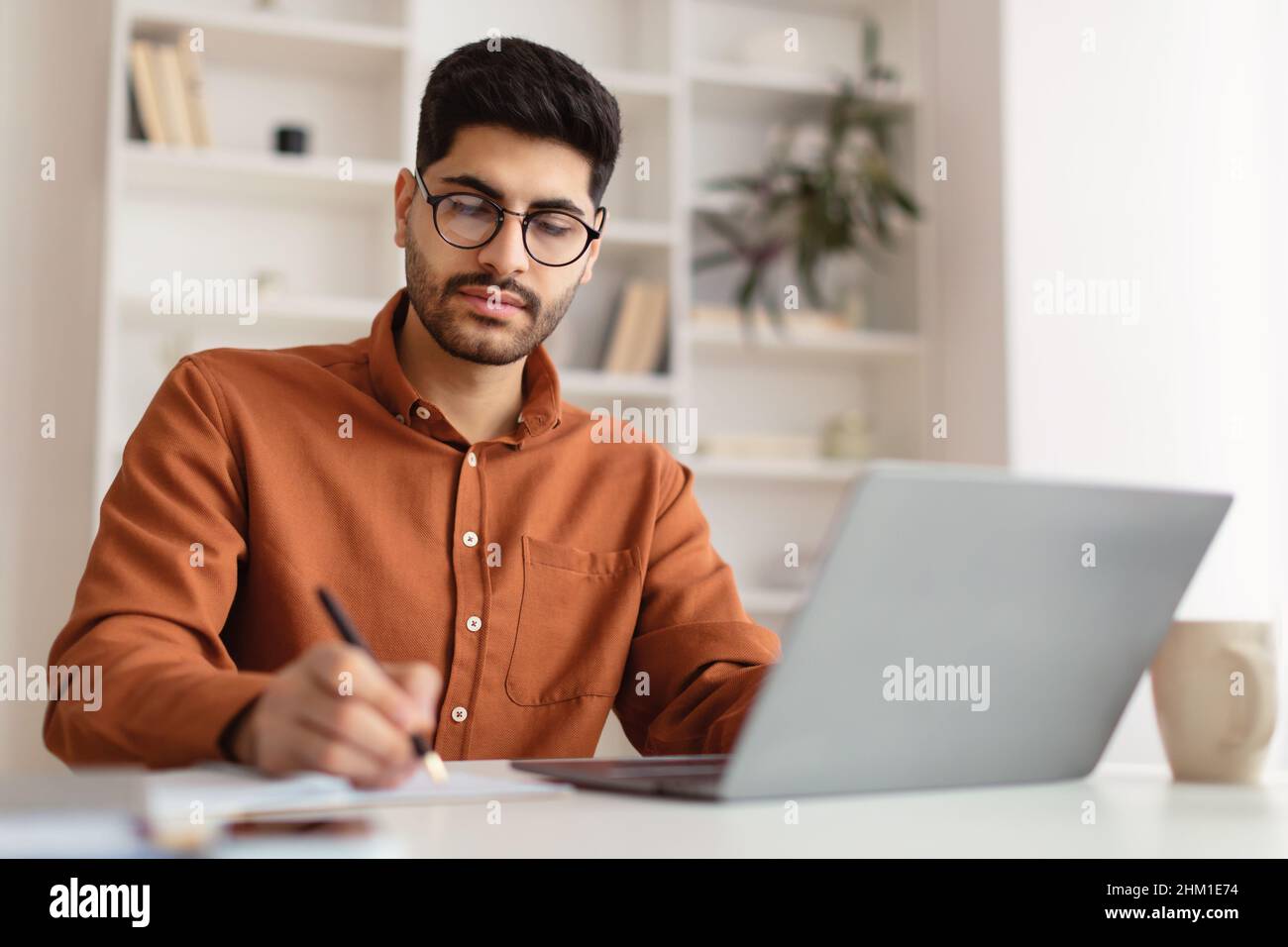 Focused Arab man in glasses using laptop and writing Stock Photo