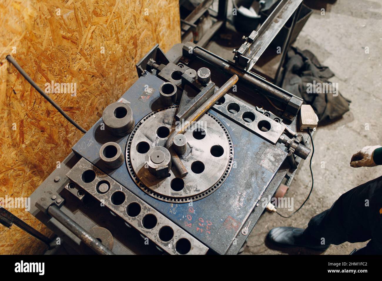 Worker at factory with industrial machine for bending of metal pipes. Stock Photo