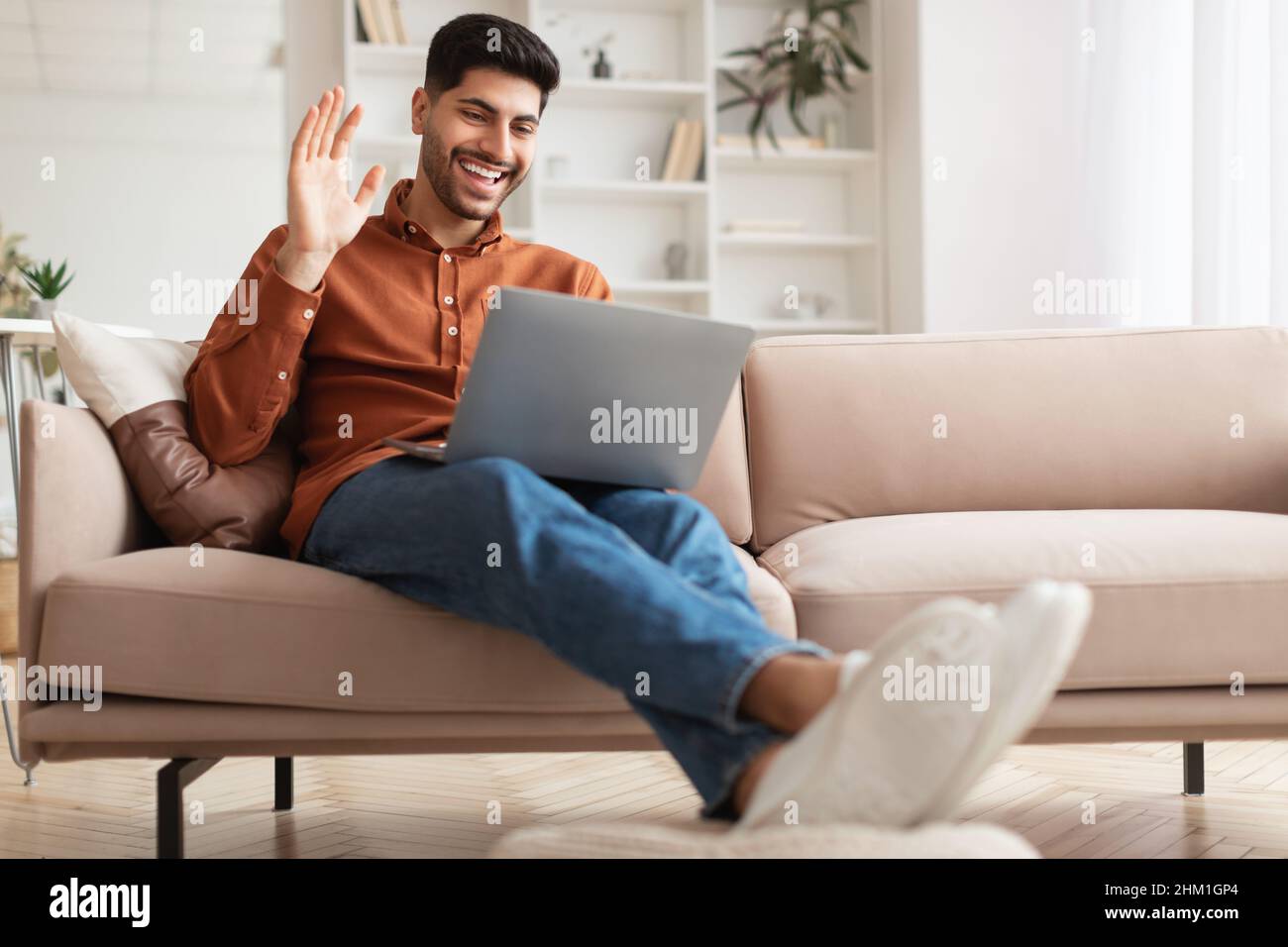 Smiling man working on laptop waving hand Stock Photo