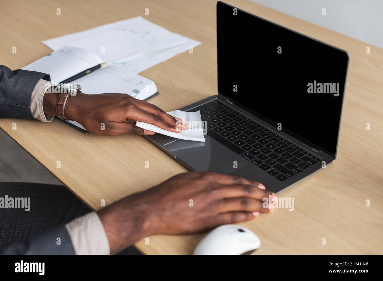 Unrecognizable African American office worker sitting ar desk, wiping laptop computer with napkin, mockup for design Stock Photo