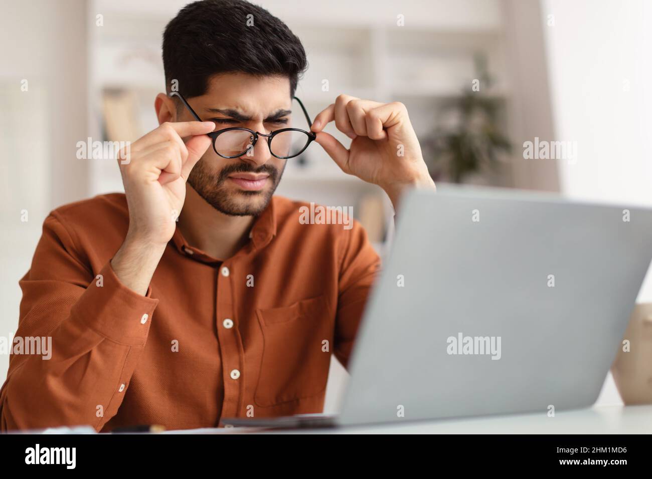 Confused Arab guy using laptop looking at screen Stock Photo