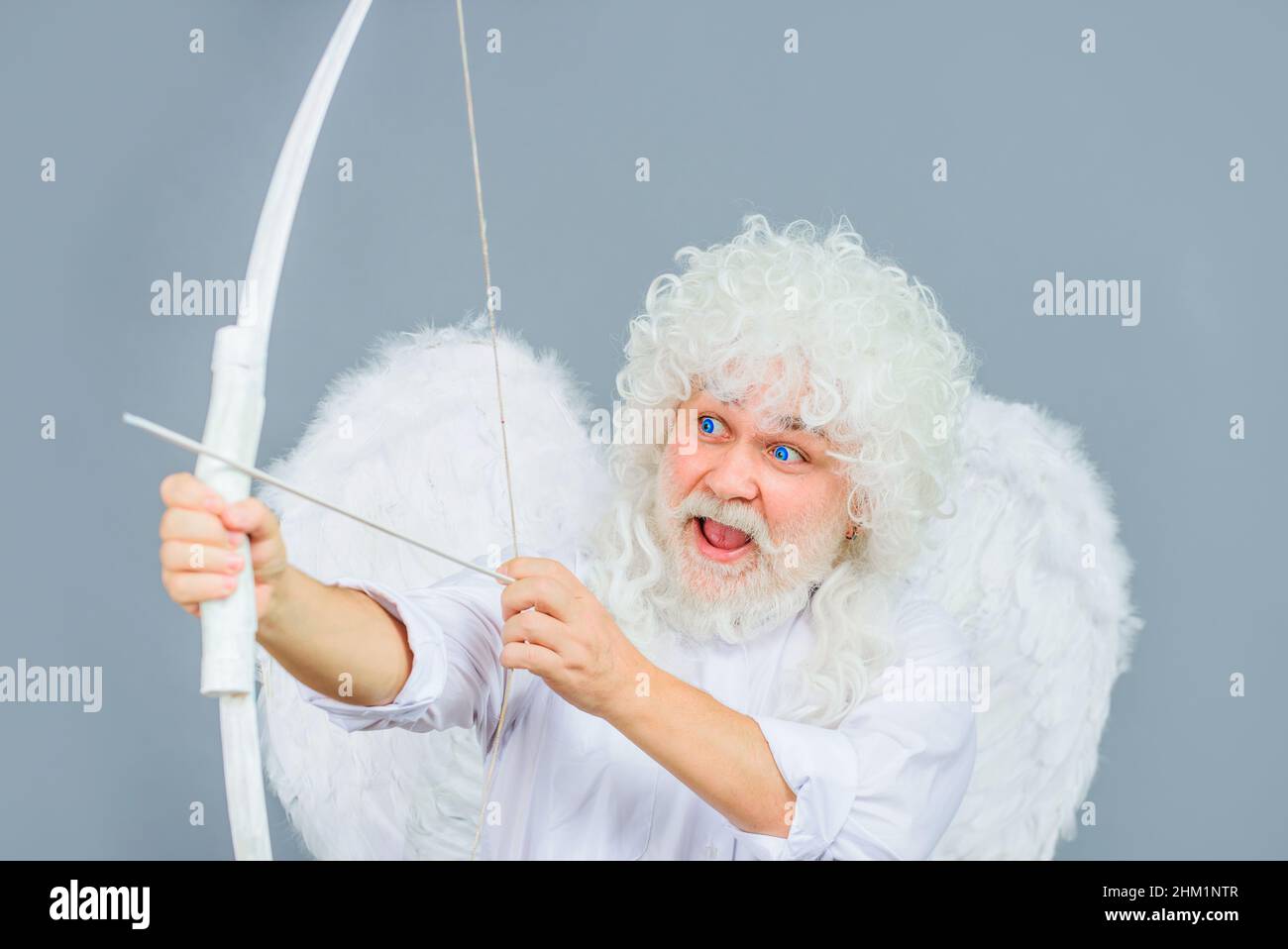 Valentines Day. Funny cupid aiming with bow and arrow. Angel with wings and white wig. Saint valentine. Stock Photo