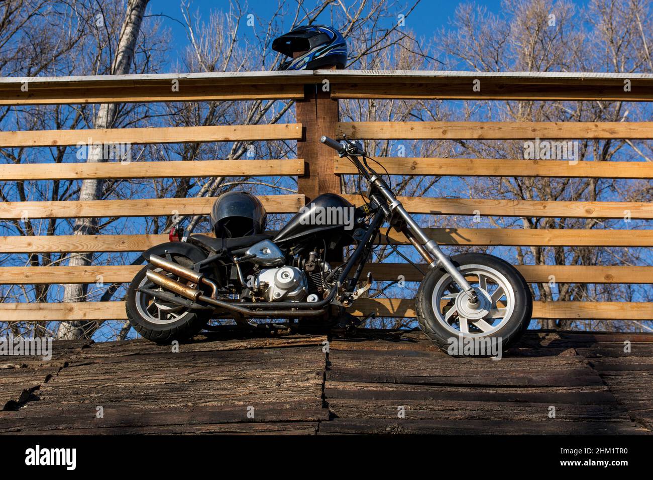 Nis, Serbia - February 06. 2022 Old black motorcycle on a wooden roof leaning against a railing and blue sky in the background on sunny day Stock Photo