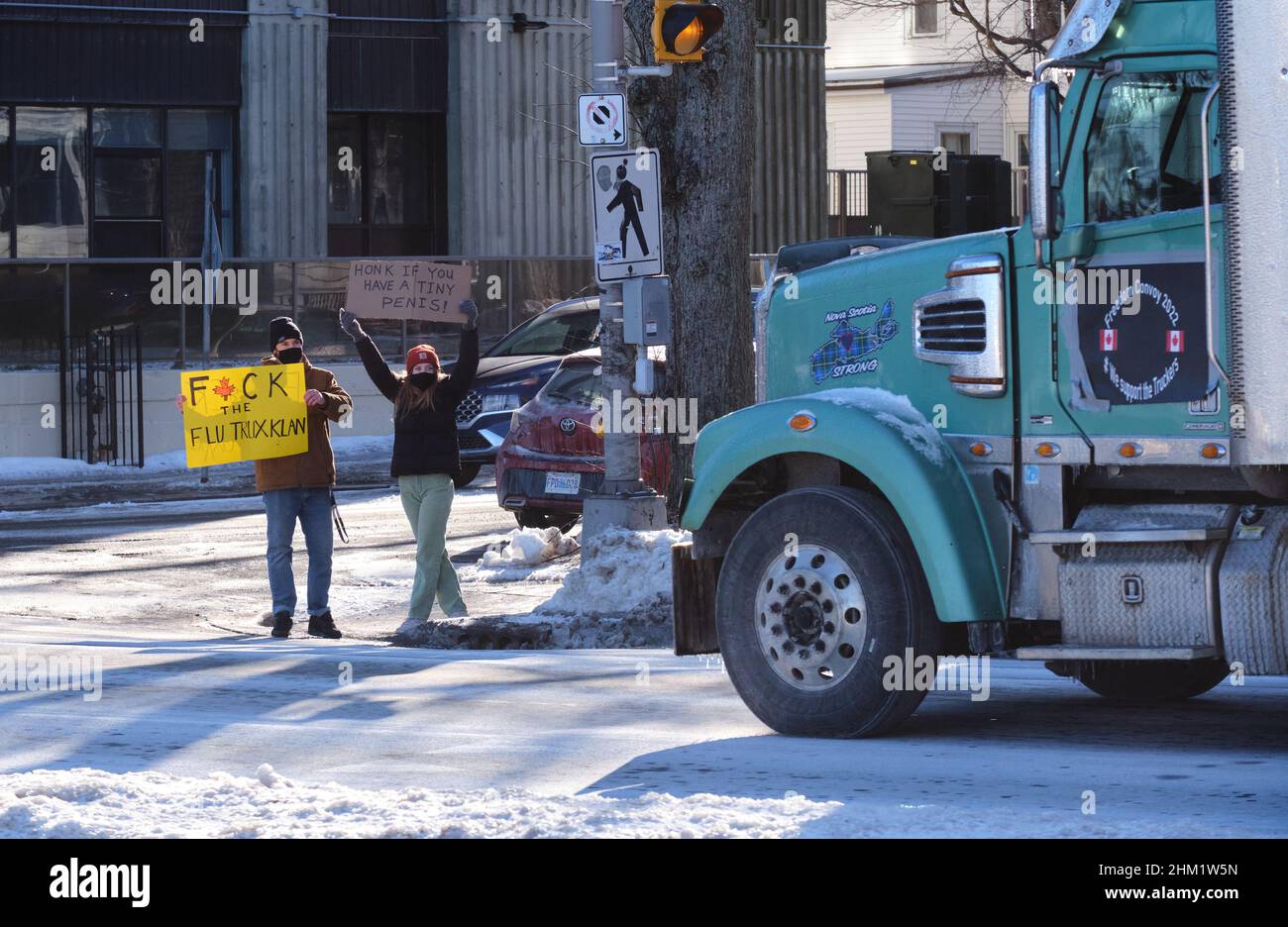 Halifax, Nova Scotia, Canada. February 6th, 2022. Two Locals protesting and forcing the Freedom Convoy to stop with signs making fun of continual honking that has been permanent in these rallies. The Freedom Convoy 2022 against all Covid-19 mandates hits the streets of Halifax, with hundreds of cars, pick-up trucks and a few trucks driving through the streets. The movement which originally went to Ottawa, and now expended to local rallies throughout the country demanding end of all mandates and measures in fight against the pandemic. Credit: meanderingemu/Alamy Live News Stock Photo