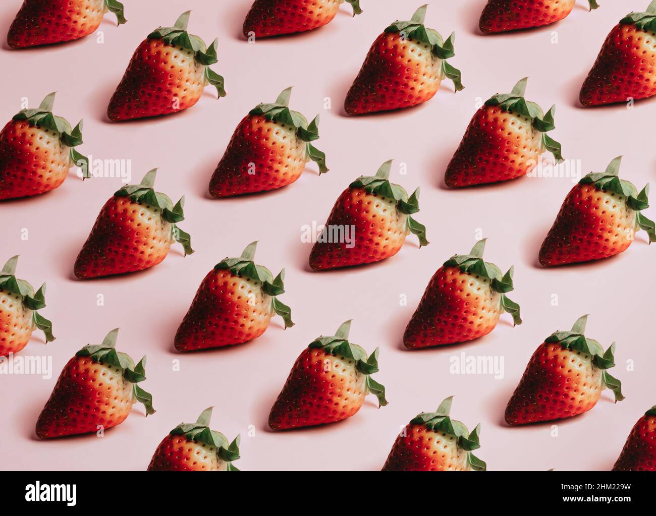 Minimal and repetitive pattern of delicious strawberries over a pastel pink background Stock Photo