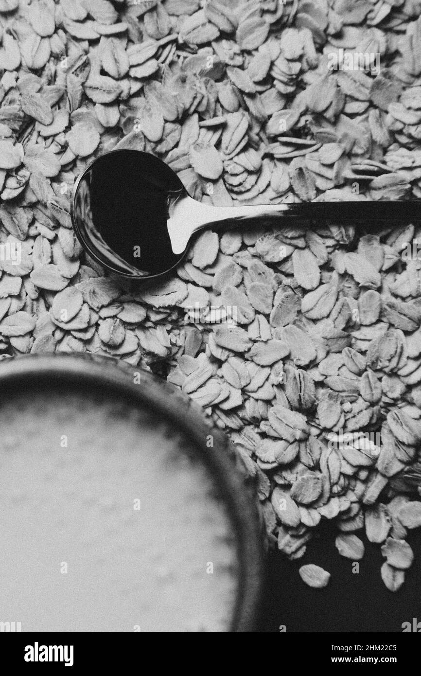 A metallic spoon over of a bunch of oat seeds with a cup of oath milk Stock Photo