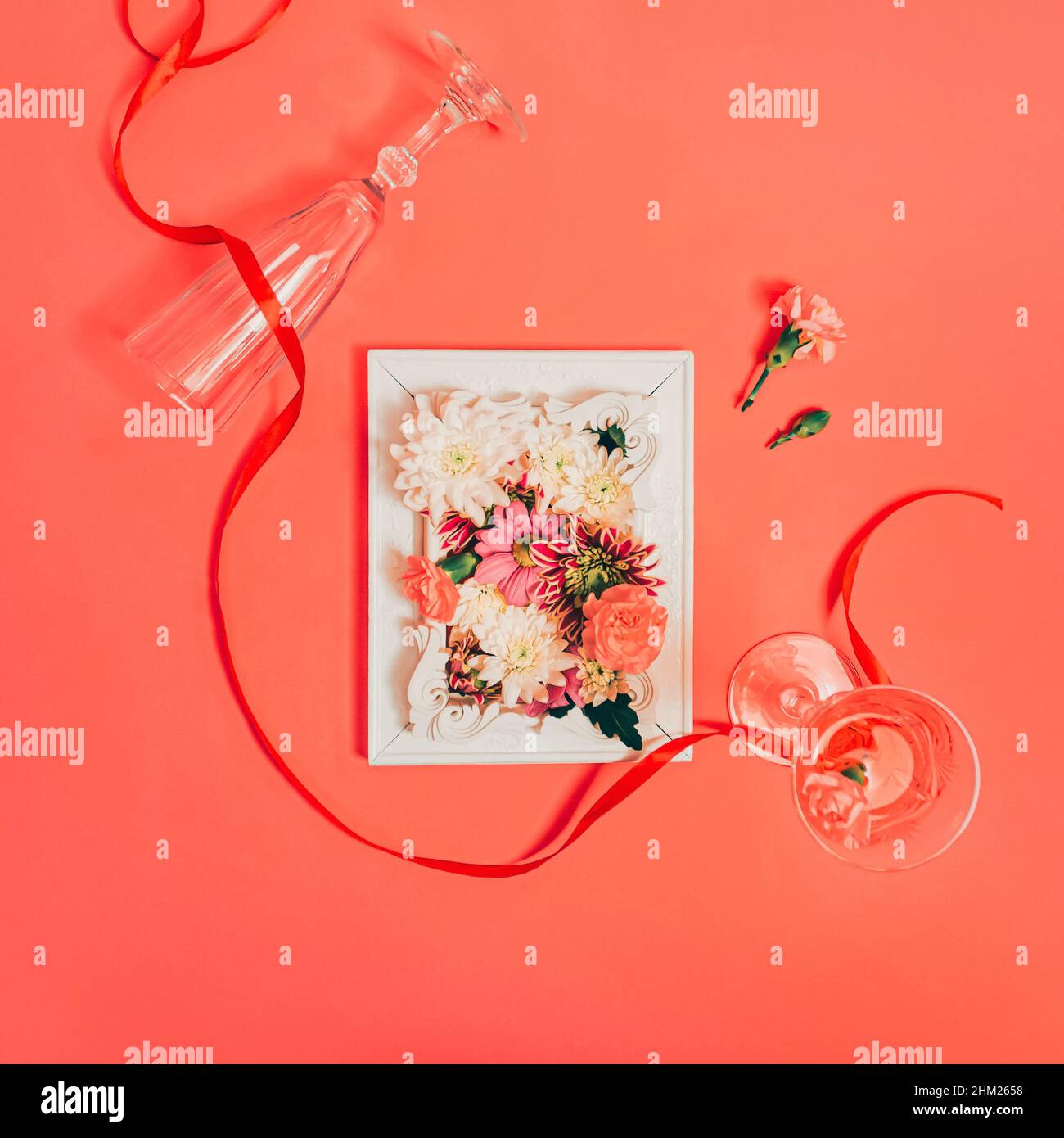 Creative composition of various flowers, champagne glasses, and renaissance frames. Elegant red satin ribbon. Flowerscape flat lay. Women's Day or mot Stock Photo