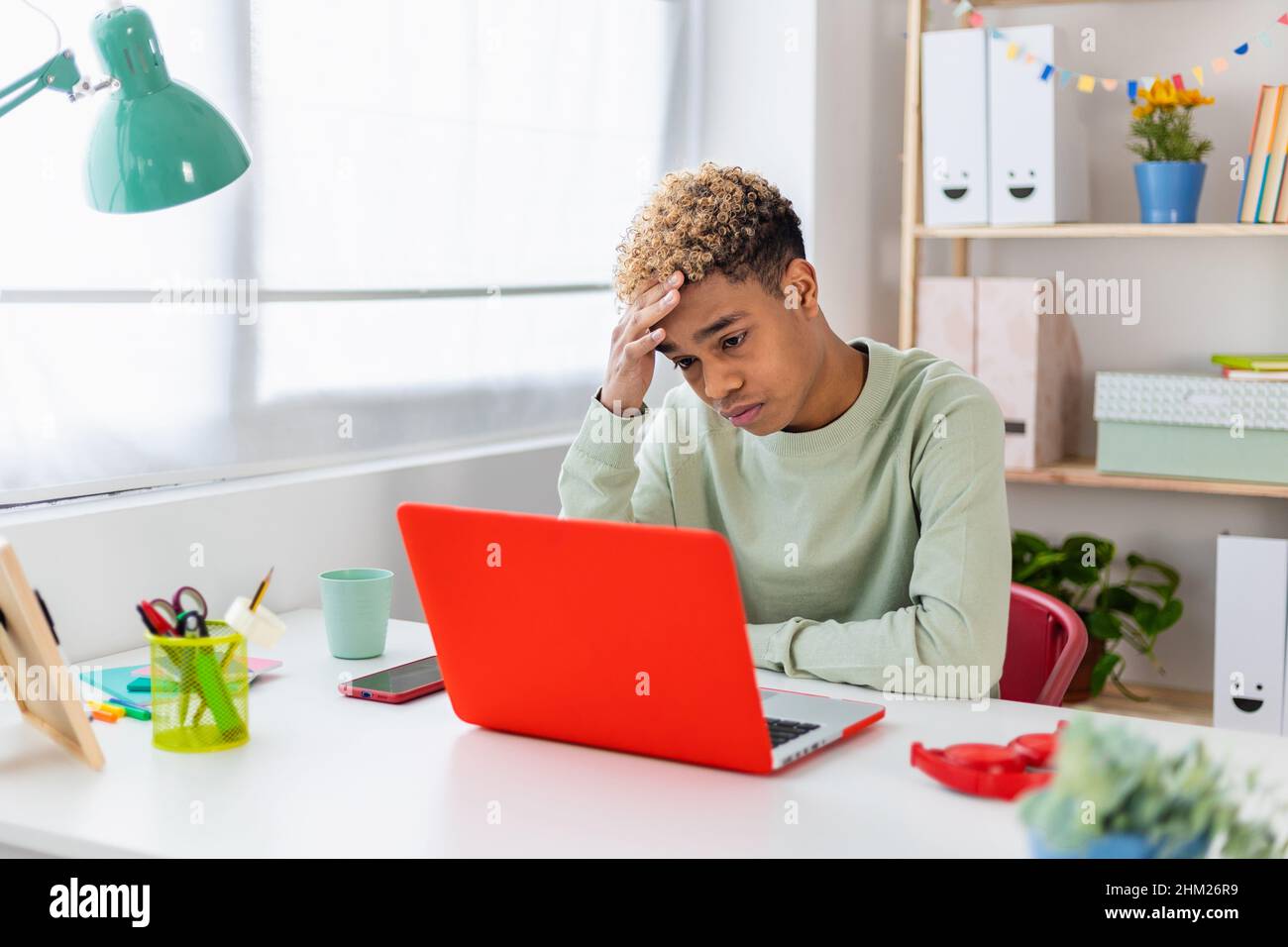 Portrait of stressed teenager boy sitting on desk in youth room Stock Photo