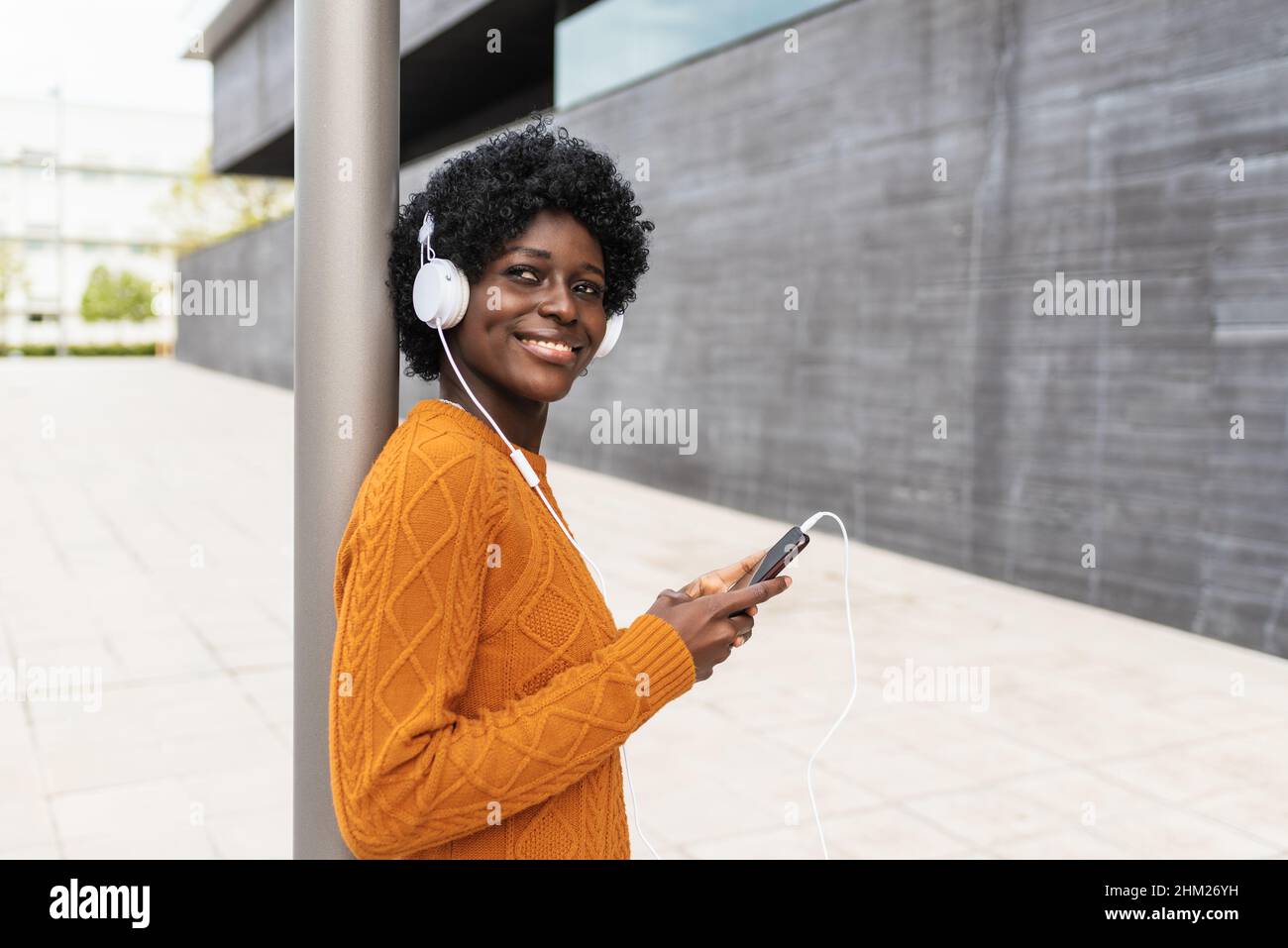 Black woman enjoying listening music with mobile phone and headphones outdoors on the street. Stock Photo