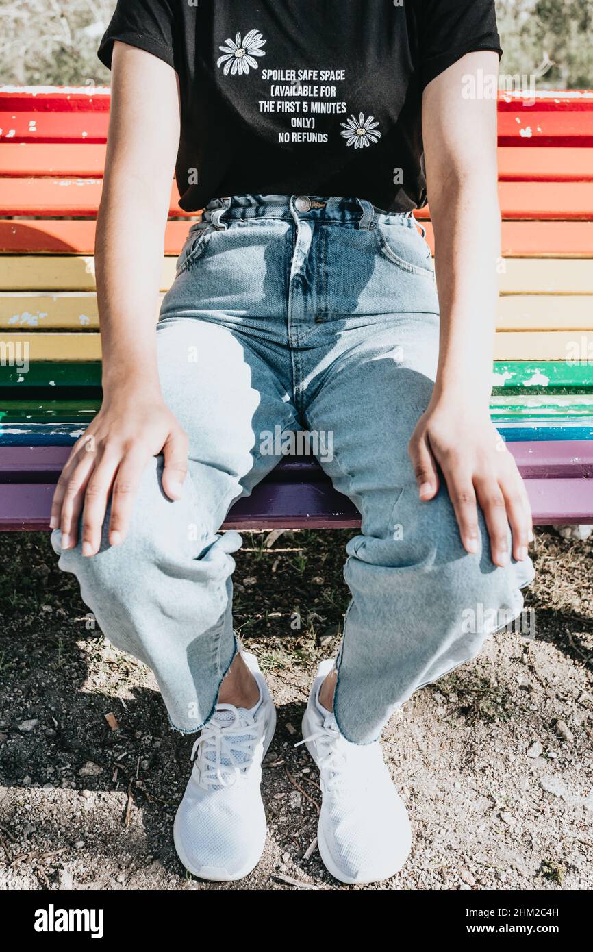 Close up of a woman wearing mom jeans over a rainbow lgbt bench at