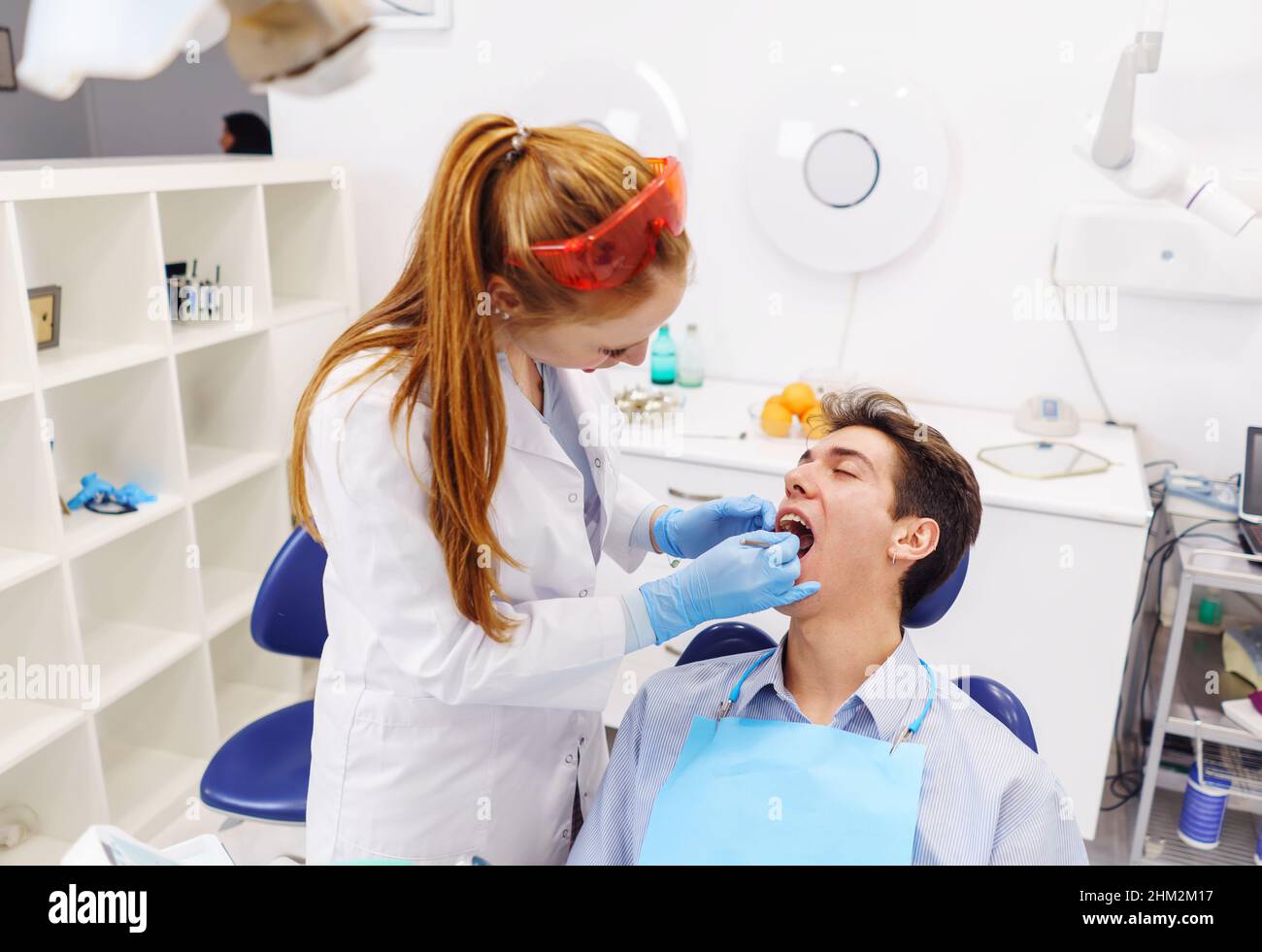 From above redhead female doctor examining teeth in opened mouth of young man while working in modern dentist office Stock Photo