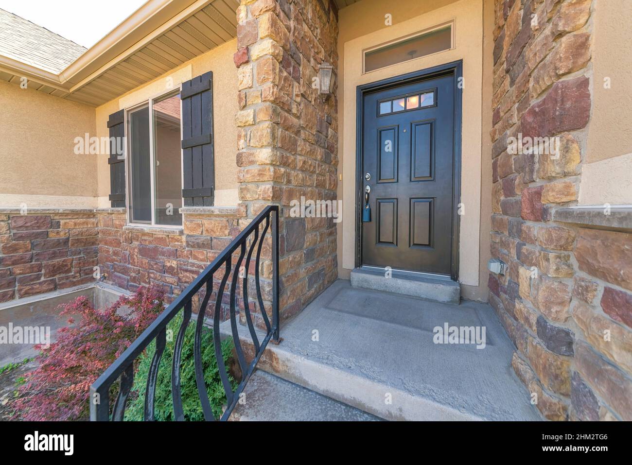 Facade of a house with brown stone veneer exterior and shrubs at the front Stock Photo