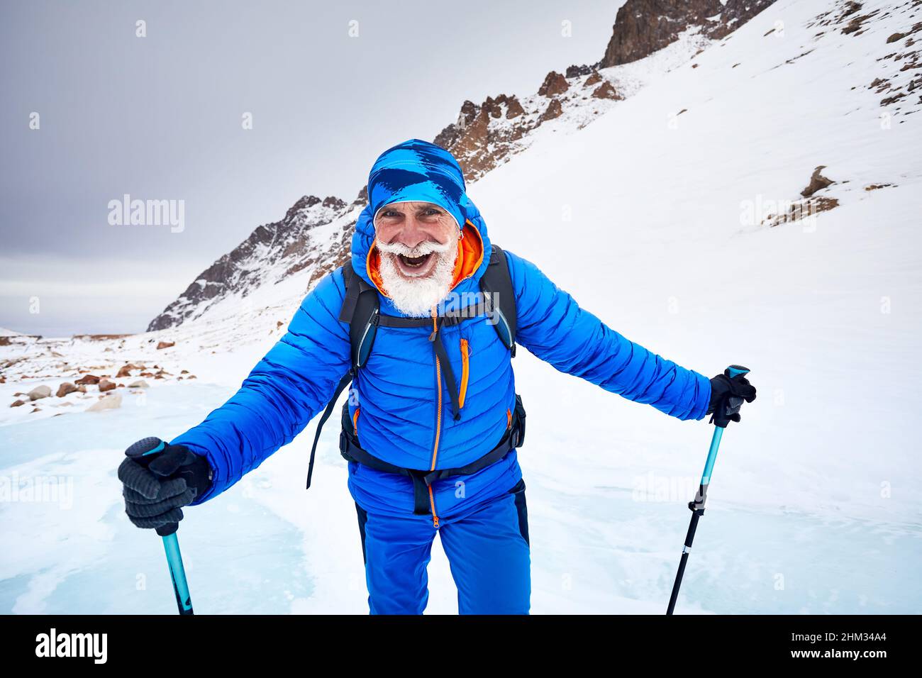 Tourist with white beard and backpack walking at blue ice glacier in beautiful landscape of mountain valley covered with snow in Almaty, Kazakhstan Stock Photo