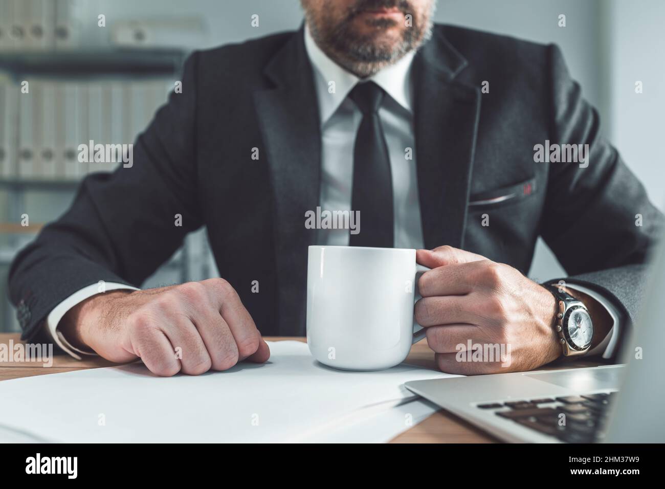 Businessman holding a white coffee cup at office desk. Coffee break for daily dose of caffeine at work, selective focus Stock Photo