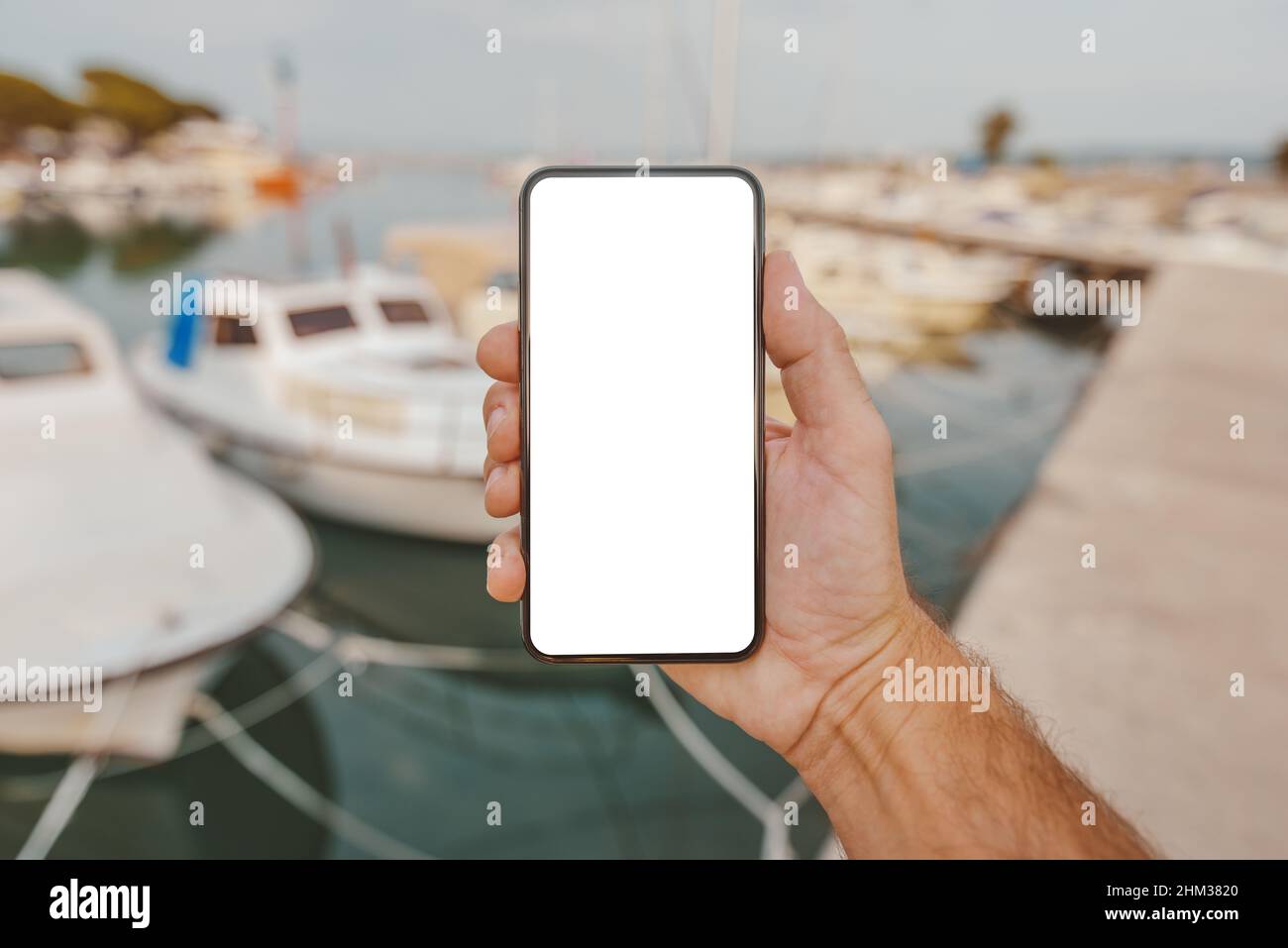 Fisherman holding smartphone with blank mock up screen in front of his boat in marina, selective focus Stock Photo