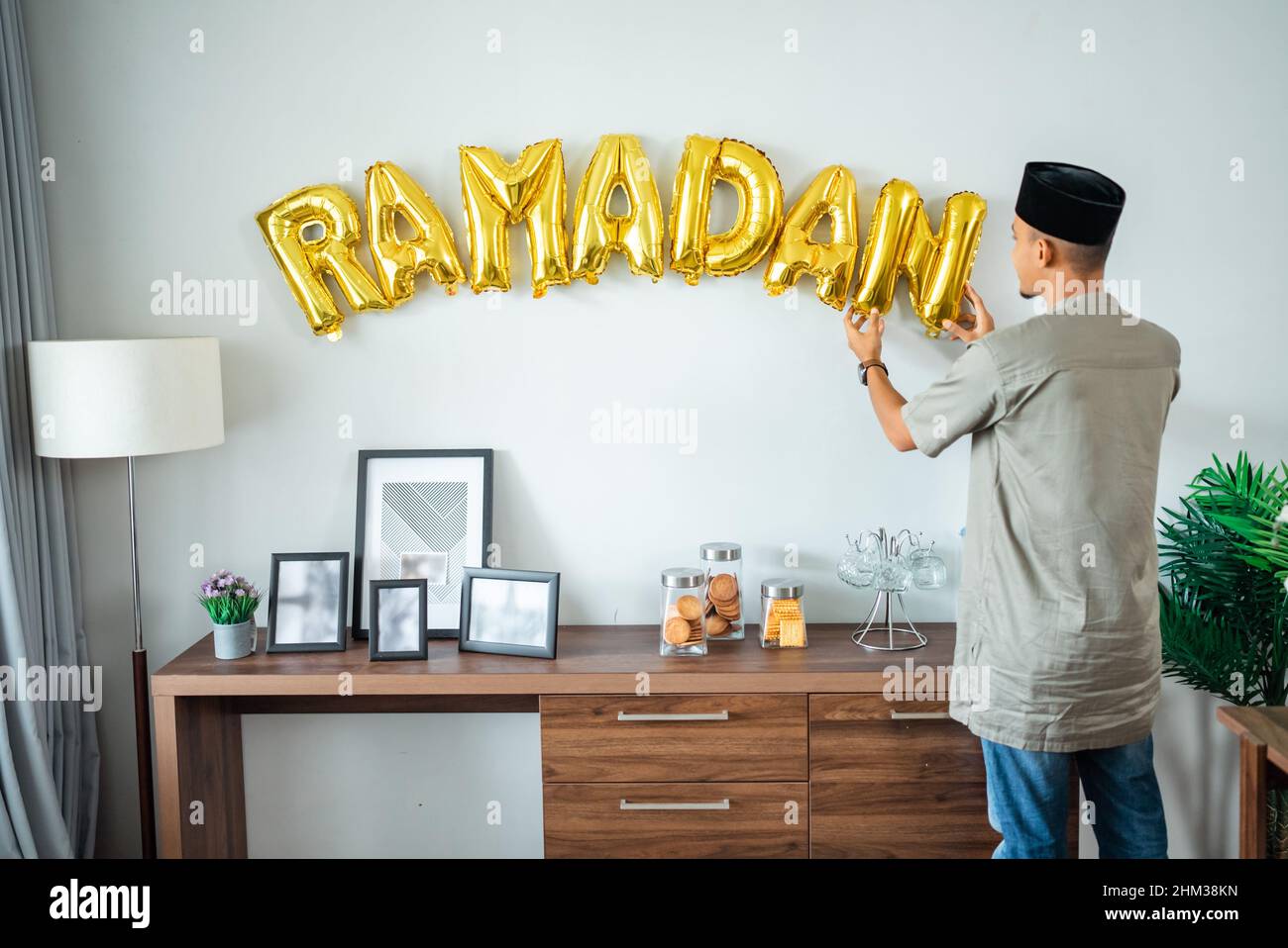 muslim male decorating the wall with ramadan balloon text Stock Photo