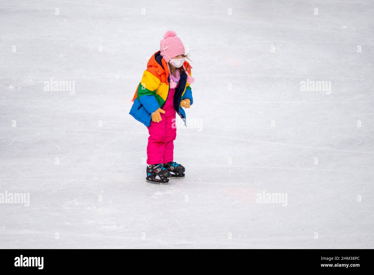 Lone little girl ice skater wearing face mask at an outdoor ice skating ...