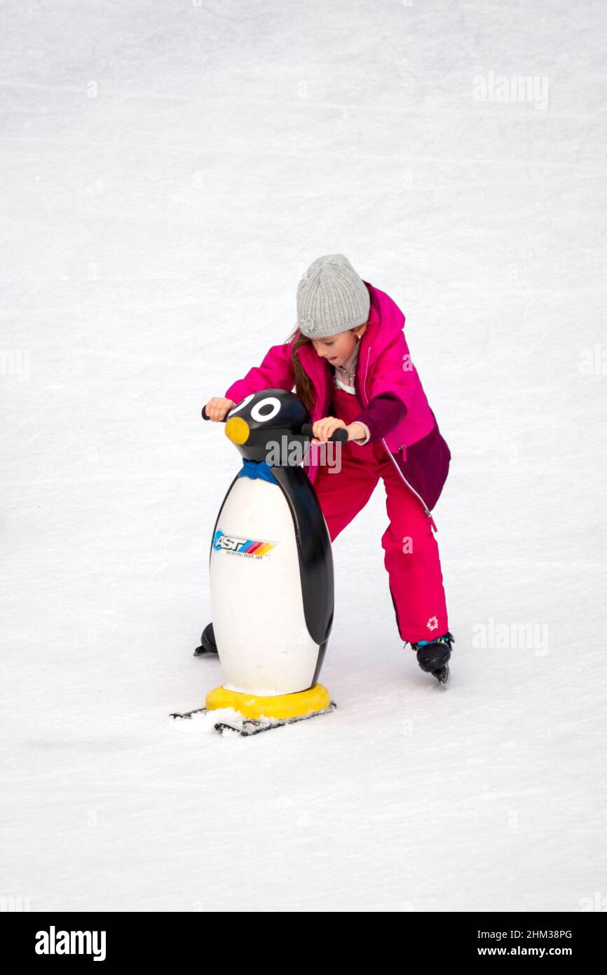Lone little girl learning to skate on ice using ski penguin ice skating aid Stock Photo