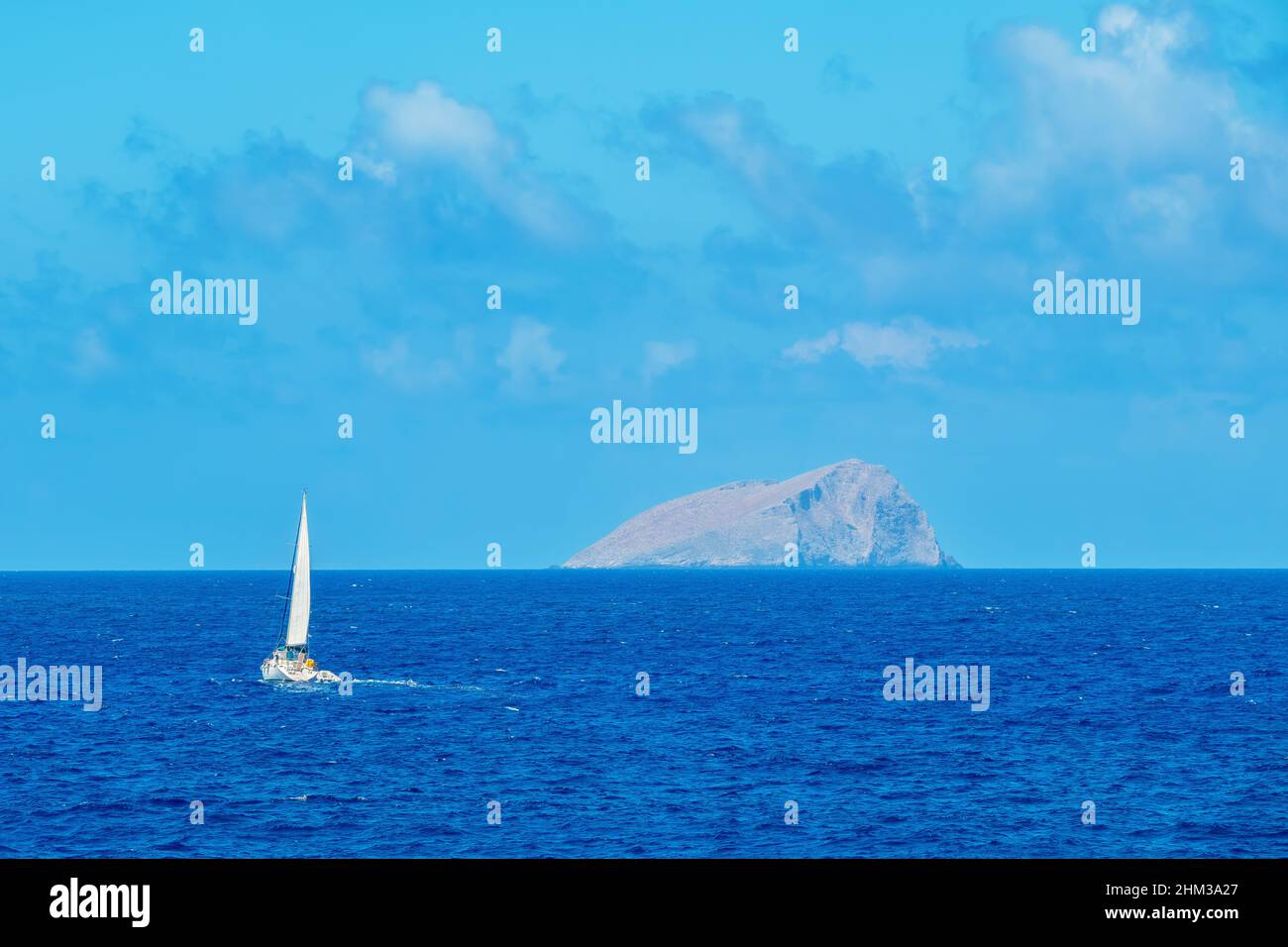 White sailed yacht sails off the rocky island Stock Photo